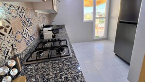 A kitchen with a gas stove, a stainless steel refrigerator, and a window with a view of the outside. - Luxury Apartment Sunset – Private Parking (Tanger)