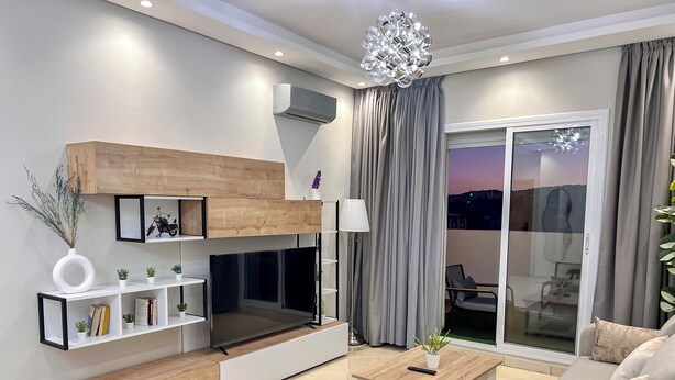 A modern living room with a sofa, a coffee table, a TV, and a fireplace. - Luxury Apartment Sunset – Private Parking (Tanger)