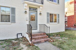 A two-story white brick building with a gray front door, a small front porch with steps, and a black metal railing.