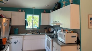 Una cucina con mobili bianchi, un lavandino, un forno a microonde e una finestra vista verde.