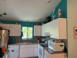 A kitchen with white cabinets, a sink, a microwave, and a window with a view of greenery.