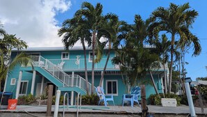 Un edificio color turchese con una scalinata, palme e sedie blu.