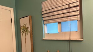 Una stanza con una parete color petrolio, un quadro con una palma, una finestra con persiane e decorazioni a forma di stella marina.