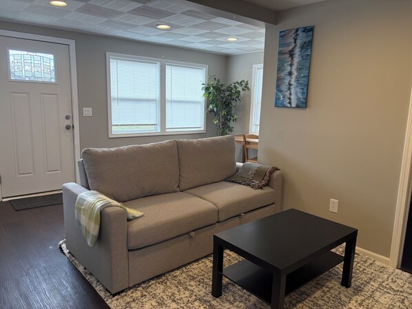 A living room with a beige sofa, a black coffee table, a door with a window, and a painting on the wall.