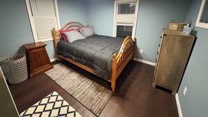 Un dormitorio con cama de madera, una mesita de noche, un aparador y una ventana con persianas.