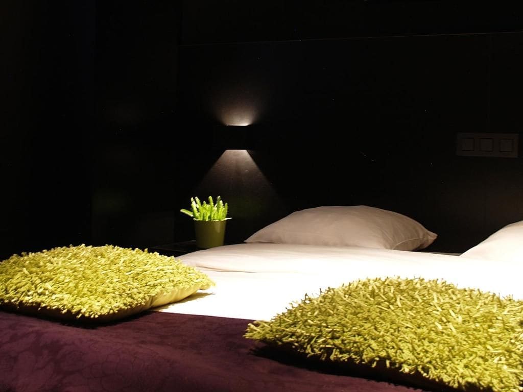 A dimly lit room with a bed, a bedside lamp, and a small green plant.