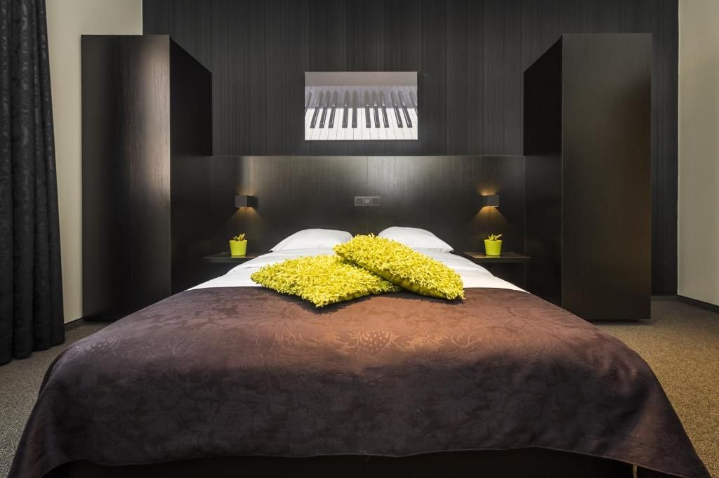 Een hotelkamer met een groot bed, twee nachtkastjes met lampen, een raam met zonwering en een wandpiano.