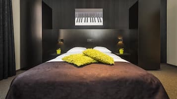 Een hotelkamer met een groot bed, twee nachtkastjes met lampen, een raam met zonwering en een wandpiano.