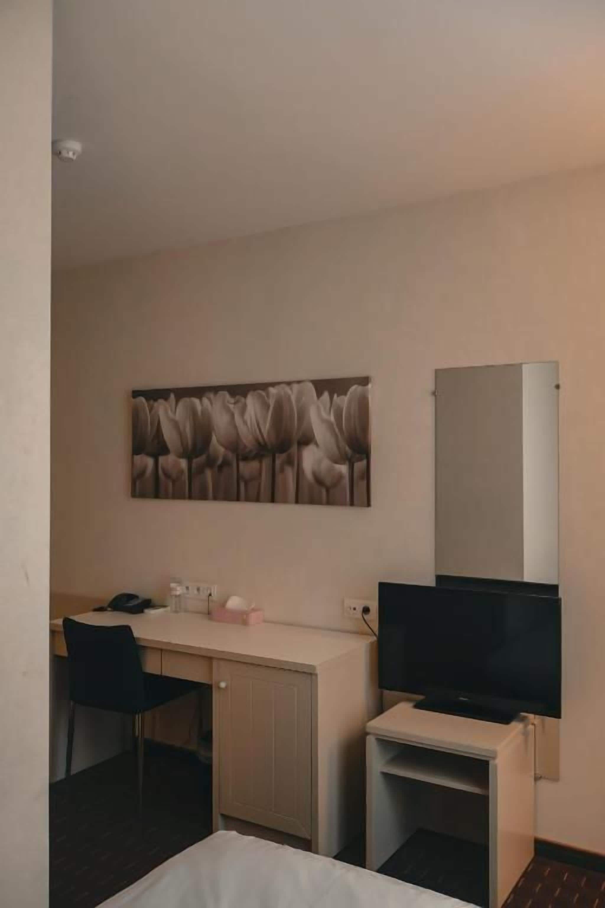 Een hotelkamer met een bed, een bureau met stoel, een televisietoestel en een schilderij aan de muur.