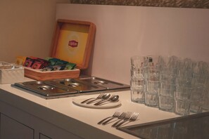 A buffet setup with a variety of food items, a Lipton tea box, and multiple glasses and forks on a table.