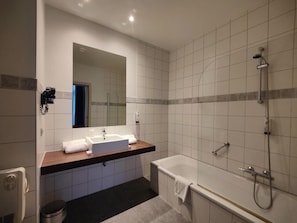 A modern bathroom with a bathtub, a shower, and a sink with a mirror above it.
