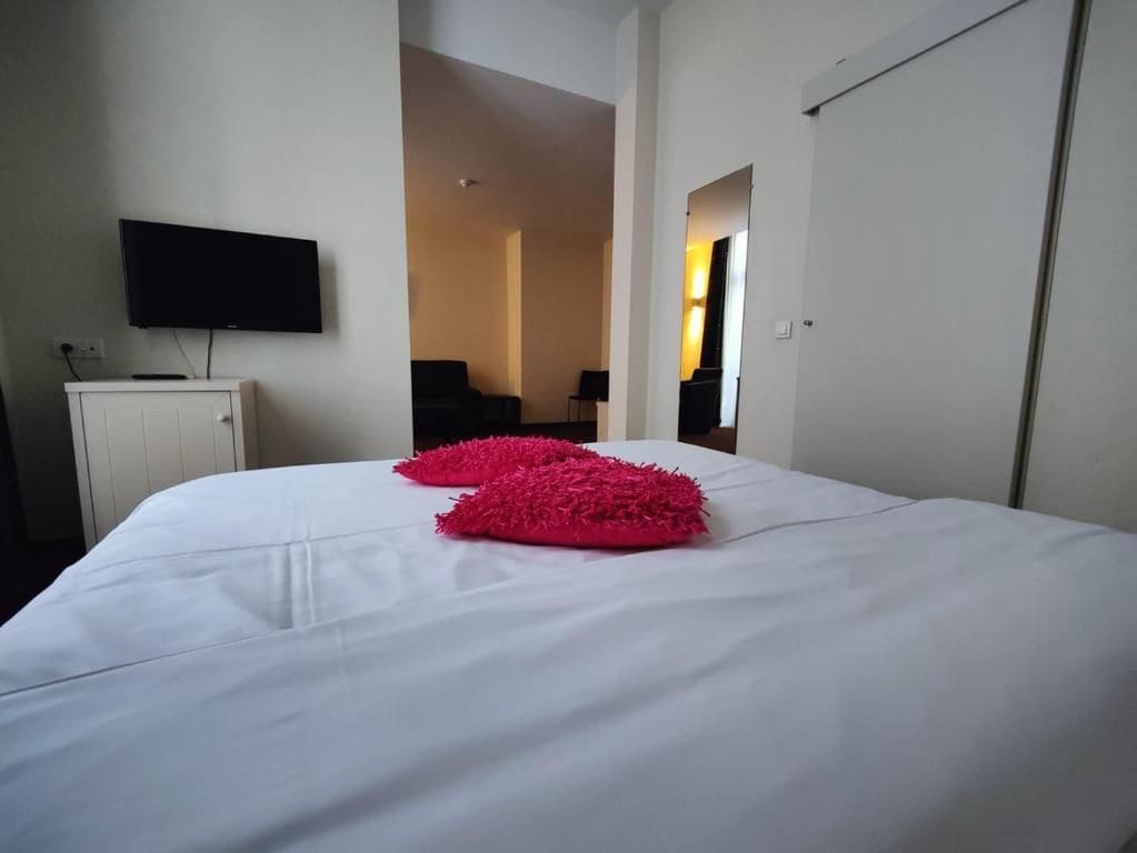 A hotel room with a bed, a television mounted on the wall, and a door leading to another room.