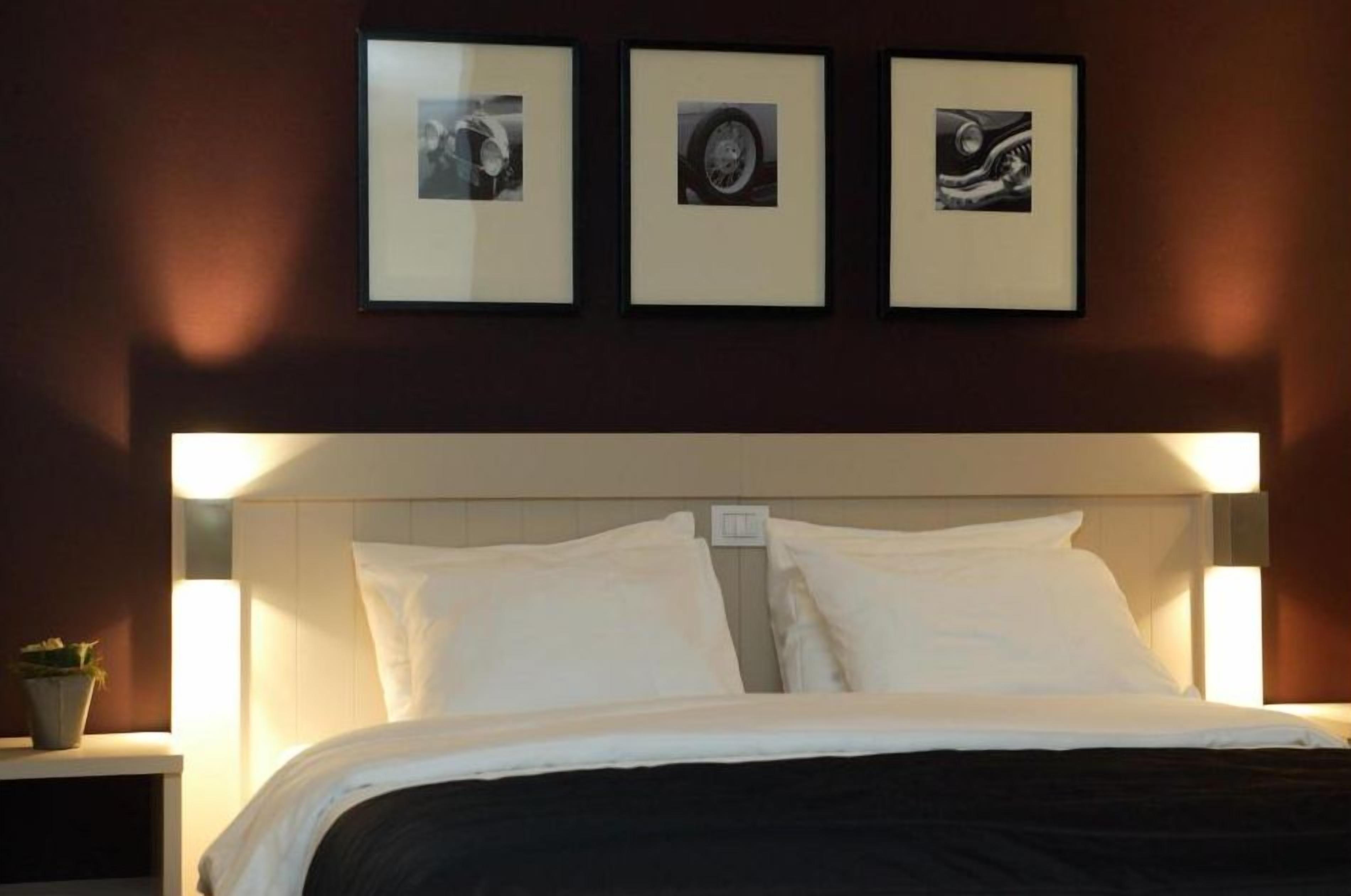 Een hotelkamer met een bed, nachtkastje en drie ingelijste foto's aan de muur.
