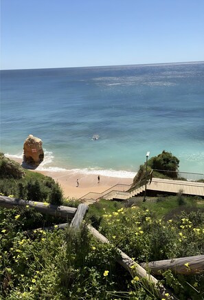 Une vue côtière avec un promontoire rocheux, une plage et une promenade en bois menant au rivage.