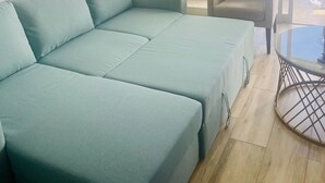 Sinivihreä sohva, pieni pyöreä pöytä ja tuoli huoneessa, jossa on suuri ikkuna ja näkymä ulos.