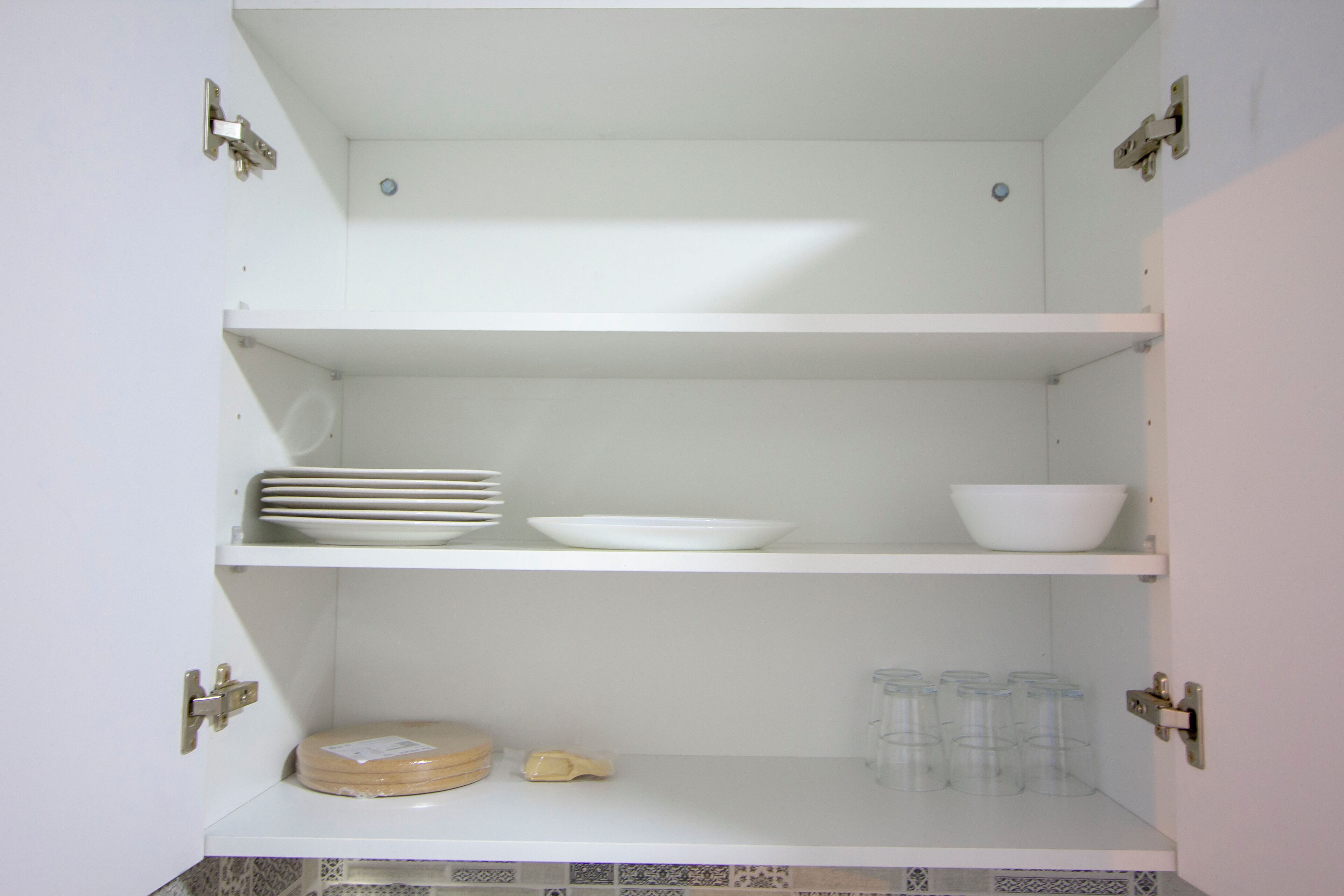 Une cuisine avec des meubles blancs, un dosseret carrelé et un plan de travail sur lequel on trouve une planche à découper, des bols et des verres.