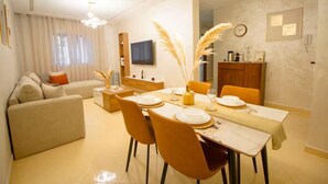 Un espace de repas moderne avec une table dressée pour quatre personnes, un canapé et un téléviseur en arrière-plan.