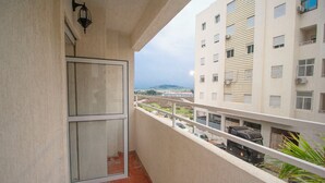 Un balcon avec une porte vitrée, donnant sur un parking, et un immeuble doté de nombreuses fenêtres et de balcons.
