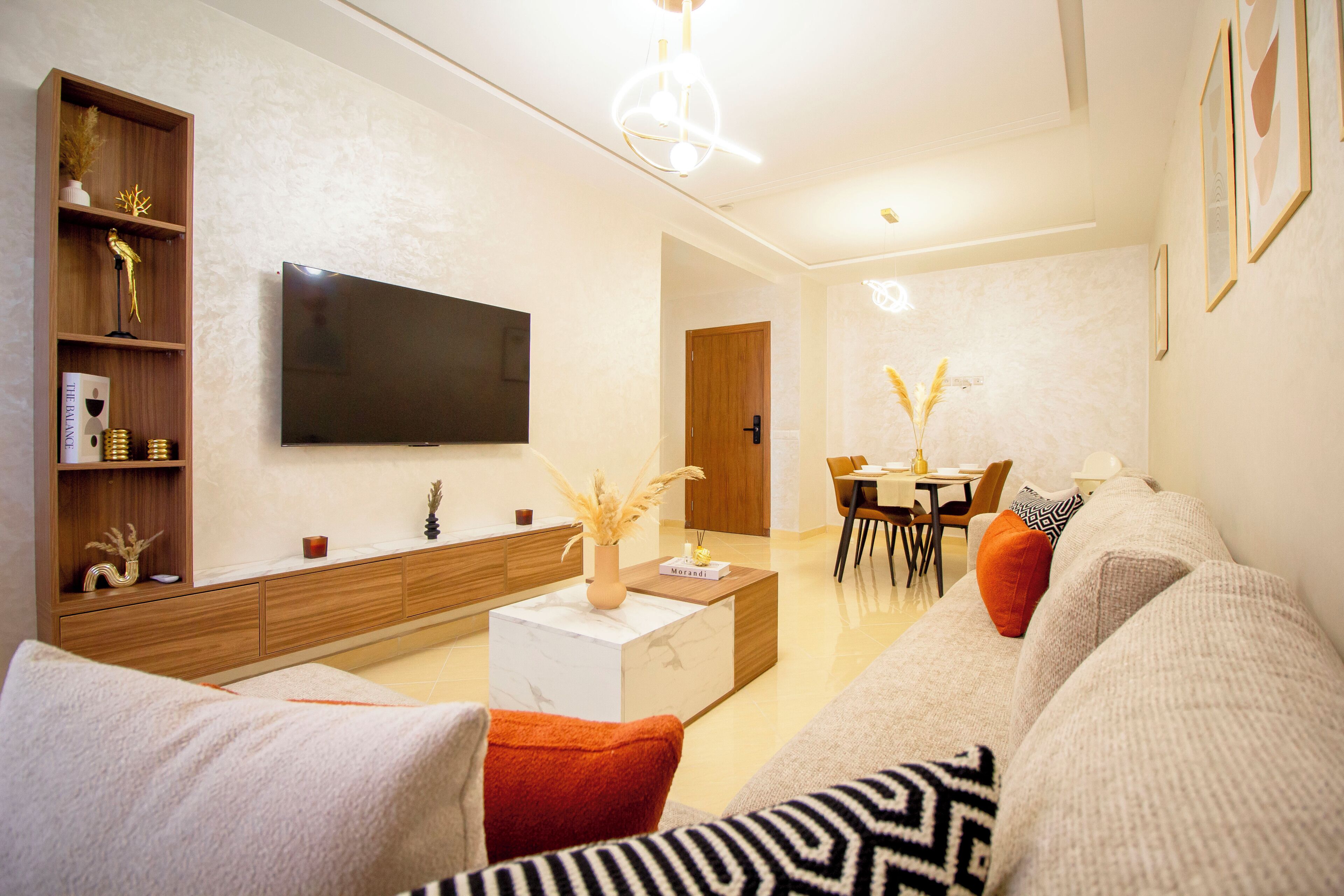 Una sala de estar moderna con un televisor de pantalla plana, un mueble de madera, una mesa de centro y un sofá con cojines decorativos.