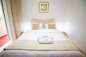 Habitación de hotel con cama, cabecera, un cuadro enmarcado en la pared y una ventana con cortinas.