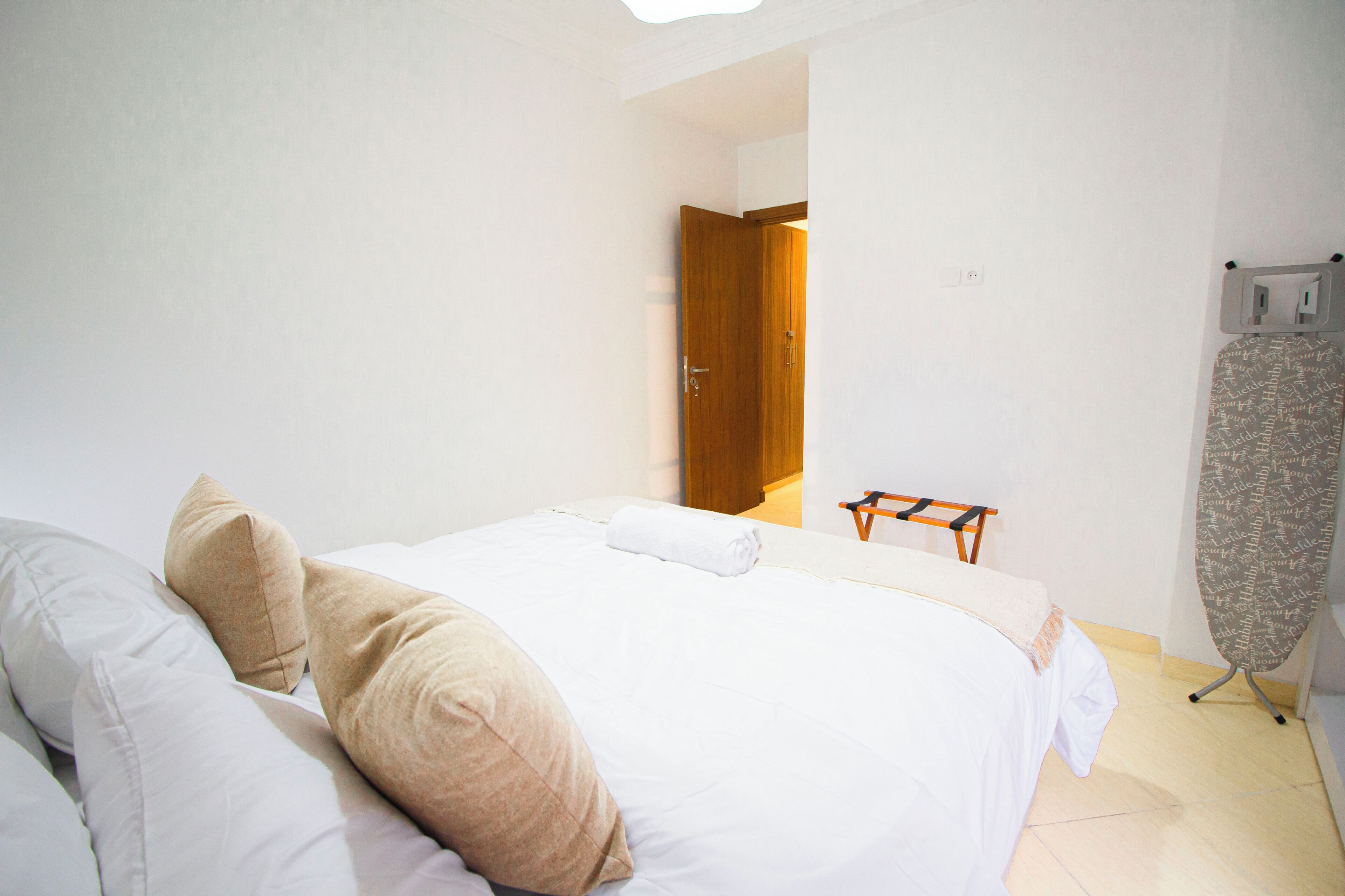 A bedroom with a bed, pillows, a wooden door, and an ironing board.