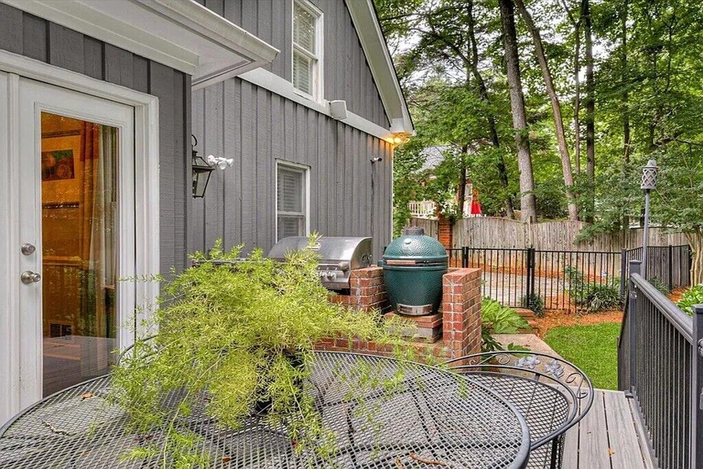 A deck with a grill and outdoor furniture, a house with a gray exterior, and a wooden fence.