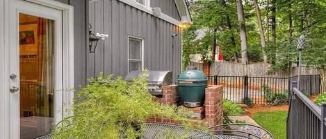 A deck with a grill and outdoor furniture, a house with a gray exterior, and a wooden fence.