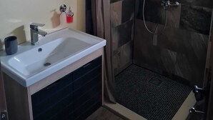 Un baño con lavamanos blanco, espejo y ducha con azulejos de piedra.