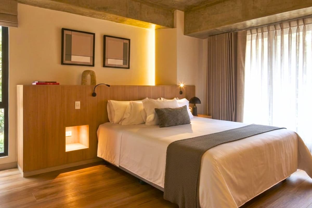 A hotel room with a large bed, a wooden headboard, a nightstand, and a window with curtains.