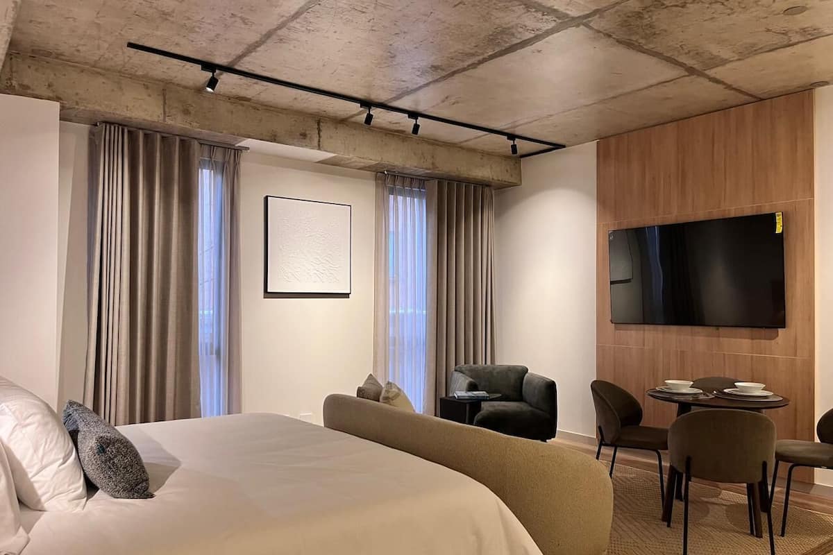 Ett modernt hotellrum med en stor säng, en platt-TV, en sittgrupp med stolar och ett matbord.