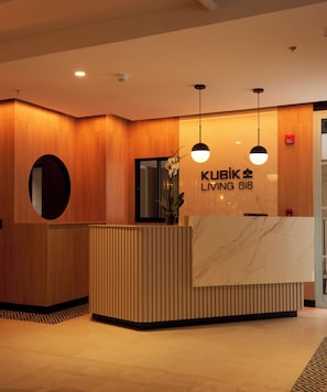 A reception desk with a marble top and wooden paneling, a sign reading 'KUBIK LIVING 818', and two pendant lights. - Kubik Living 8i8 (Bogota)
