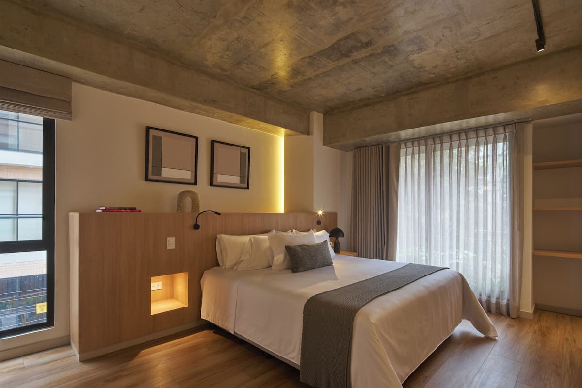 Ett modernt hotellrum med en stor säng, trägolv, ett inbyggt skrivbord och ett fönster med utsikt.