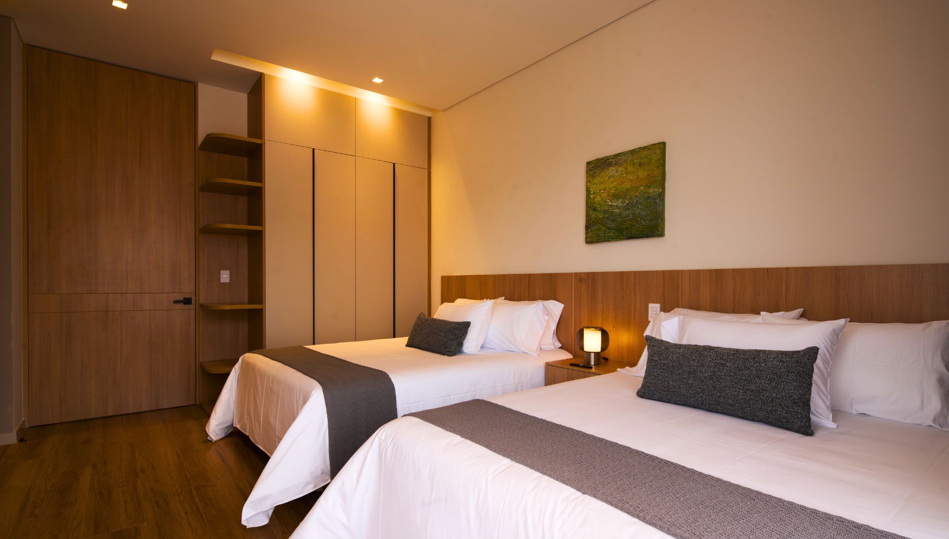 Habitación de hotel con dos camas, un armario, un cuadro en la pared y una mesita de noche con lámpara.