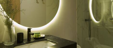 Een badkamer met een zwart wastafel, een spiegel met ronde verlichting, en een vaas met planten.