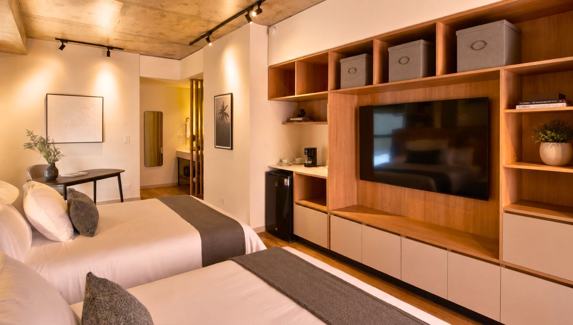 A modern hotel room with a large TV, wooden shelving, and two beds.