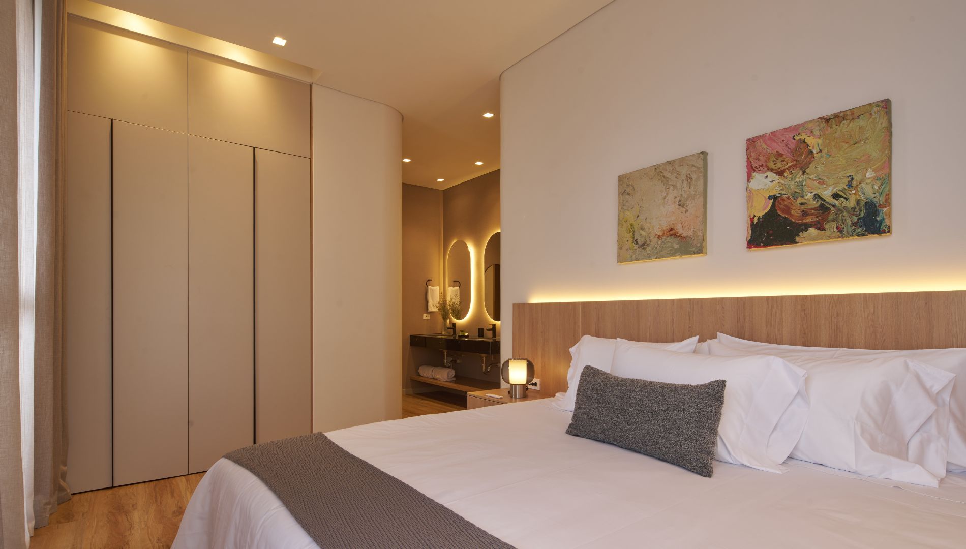 A hotel room with a bed, a wardrobe, a bathroom with a mirror, and two paintings on the wall.