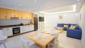 Una cocina moderna con armarios de madera, una mesa de comedor preparada para cuatro personas y una sala de estar con sofá y televisor.