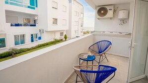 Un balcón con dos sillas azules, una mesita y vistas a edificios cercanos.