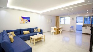 Una sala de estar moderna con un sofá azul, una mesa de centro de madera y un comedor con sillas blancas.