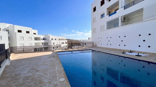 Un edificio moderno con piscina, paredes blancas y un cielo azul despejado.