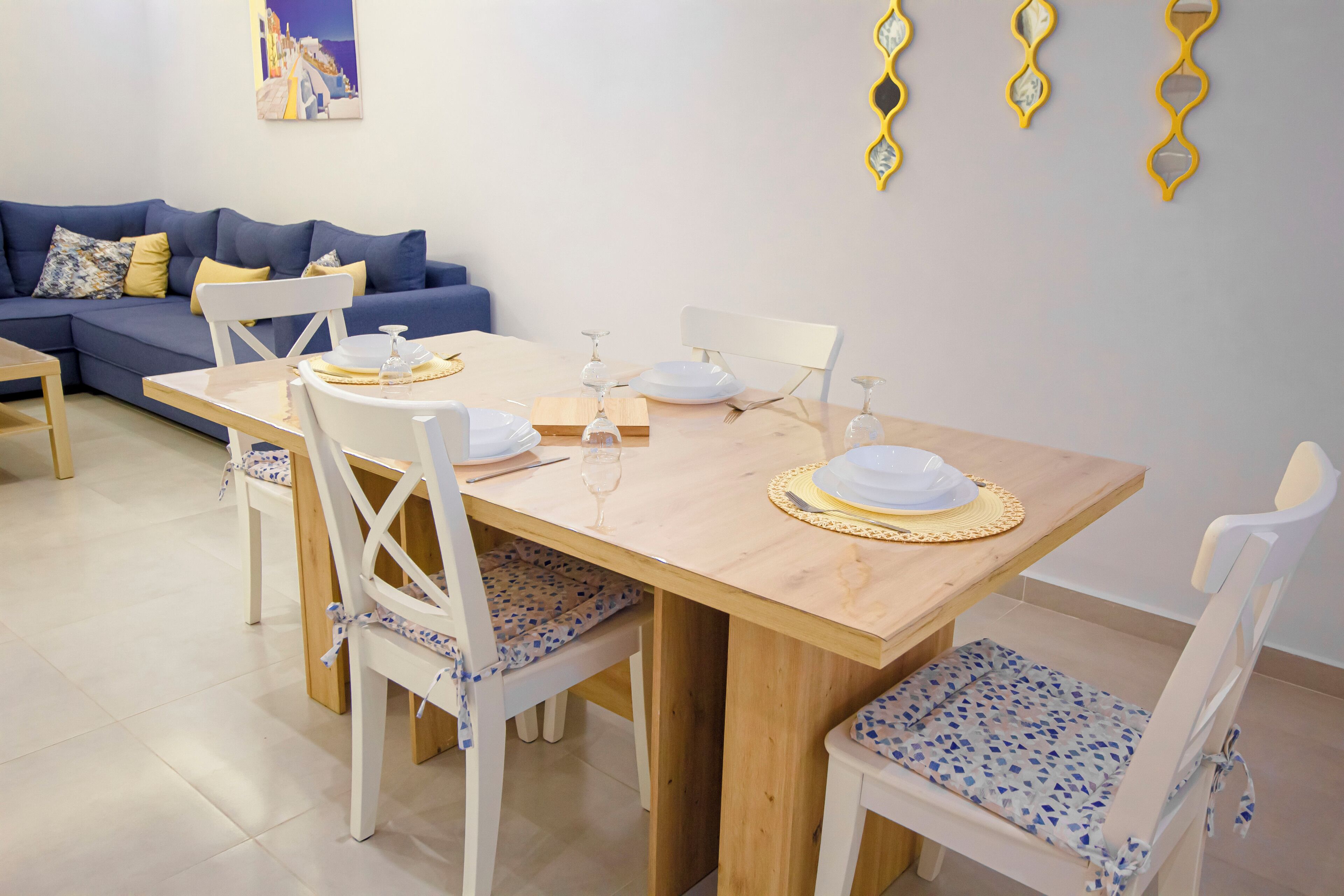 Un coin repas avec une table en bois, des chaises blanches et un canapé bleu en arrière-plan.