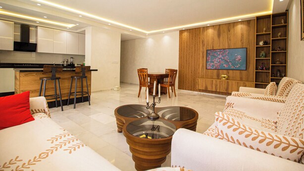 A modern living room with a sofa, a coffee table, a dining table with chairs, a kitchen area, and a wooden cabinet with decorative items. - Luxury 2-Bedroom Pool, Quiet & Spacious (Tanger)