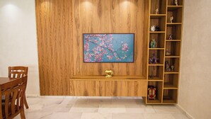 A room with a wooden wall panel, a TV mounted on it, a wooden shelf with decorative items, and a dining table with chairs. - Luxury 2-Bedroom Pool, Quiet & Spacious (Tanger)
