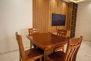 A dining area with a wooden table and chairs, a wooden wall panel, and a framed picture. - Luxury 2-Bedroom Pool, Quiet & Spacious (Tanger)