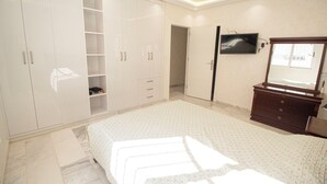 A bedroom with a bed, a wardrobe, a dresser, a television, and a mirror. - Luxury 2-Bedroom Pool, Quiet & Spacious (Tanger)