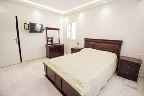 A bedroom with a bed, a dresser, a nightstand, a TV mounted on the wall, and a window. - Luxury 2-Bedroom Pool, Quiet & Spacious (Tanger)