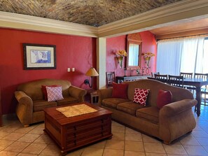 A living room with two sofas, a coffee table, a lamp, a framed picture, and a dining area with a table and chairs. - Comfortable Beachfront Condo Las Palmas II 11 B (Puerto Peñasco)