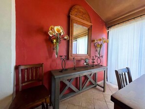 A dining area with a wooden table, chairs, a console table with decorative items, and a mirror on a red wall. - Comfortable Beachfront Condo Las Palmas II 11 B (Puerto Peñasco)