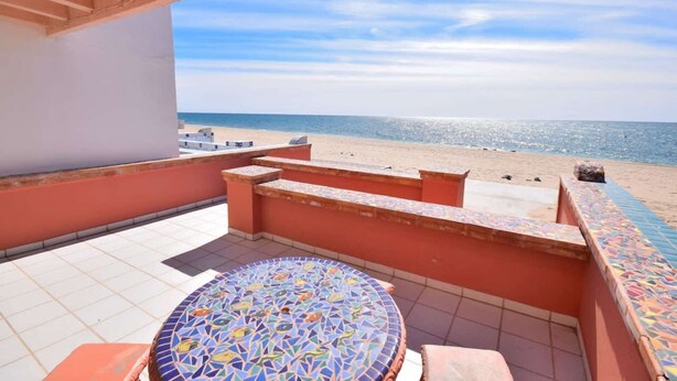 Ein Balkon mit einem gefliesten Tisch und Stühlen, Blick auf den Strand und einem klaren Himmel.