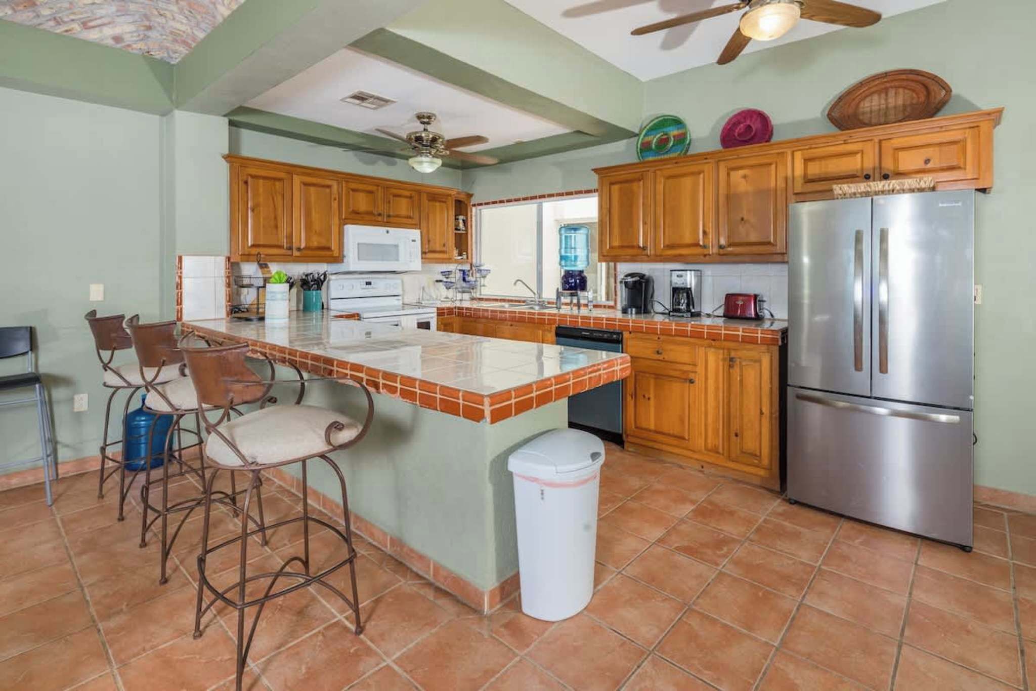 A kitchen with wooden cabinets, a stainless steel refrigerator, a bar stool, and a ceiling fan.